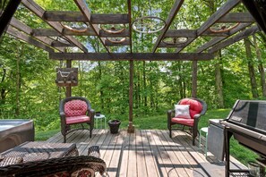 Una terraza de madera con mobiliario de mimbre, una parrilla y un pérgola decorada con una rueda de bicicleta.