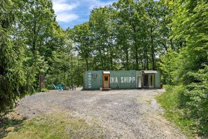 Una pequeña estructura de contenedor verde con una puerta, rodeada de grava y árboles.