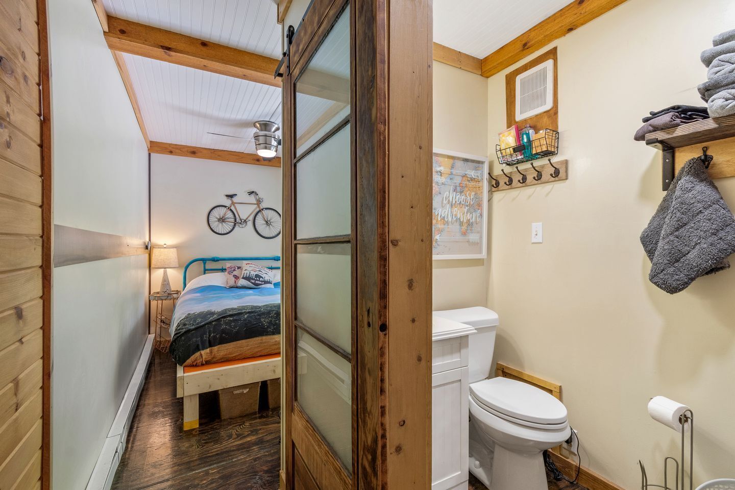 Ein kleines Zimmer mit Bett, einem Fahrrad, einer Toilette und einem kleinen Regal mit Handtüchern.
