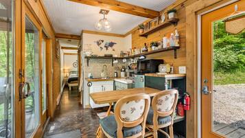A cozy cabin interior with a wooden dining table, two chairs, a kitchen area with a microwave, and a world map on the wall.