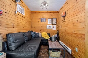 A cozy cabin interior with a black leather sofa, a small wooden table, and a wall-mounted shelf with various items.