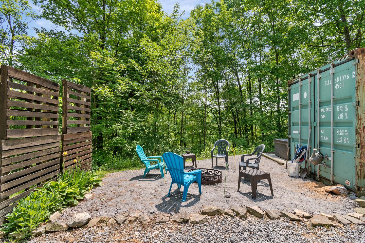 Eine Pflasterterrasse mit Sitzgelegenheiten im Freien, ein Holzzaun und ein grüner Container.