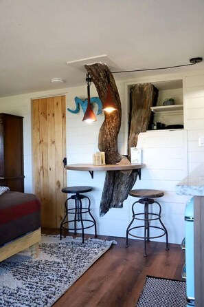Una habitación acogedora con cama, una mesita, dos taburetes y un estante original hecho con un tocón de árbol.