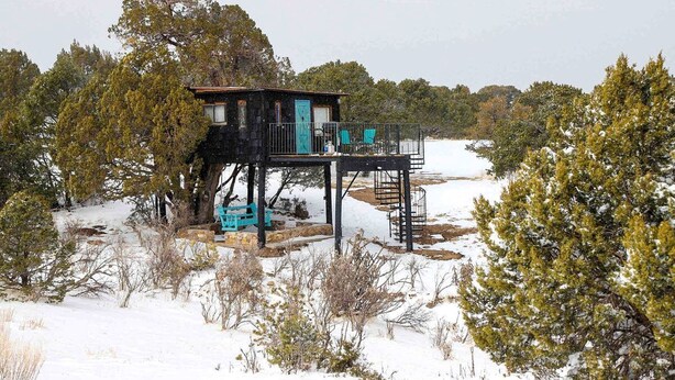 A cabin with a balcony, surrounded by trees and snow.