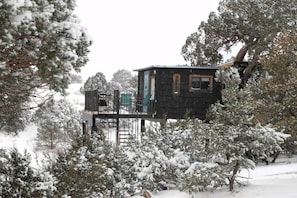 Una cabaña con terraza, rodeada de árboles cubiertos de nieve.