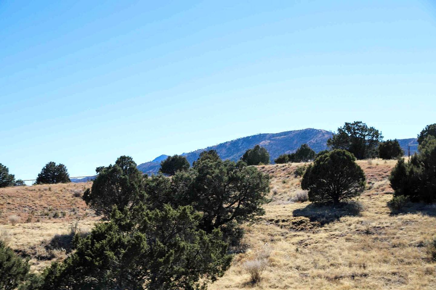 A natural landscape with a hill, trees, and a clear sky.