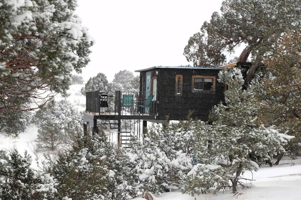 A cabin with a deck, surrounded by snow-covered trees.