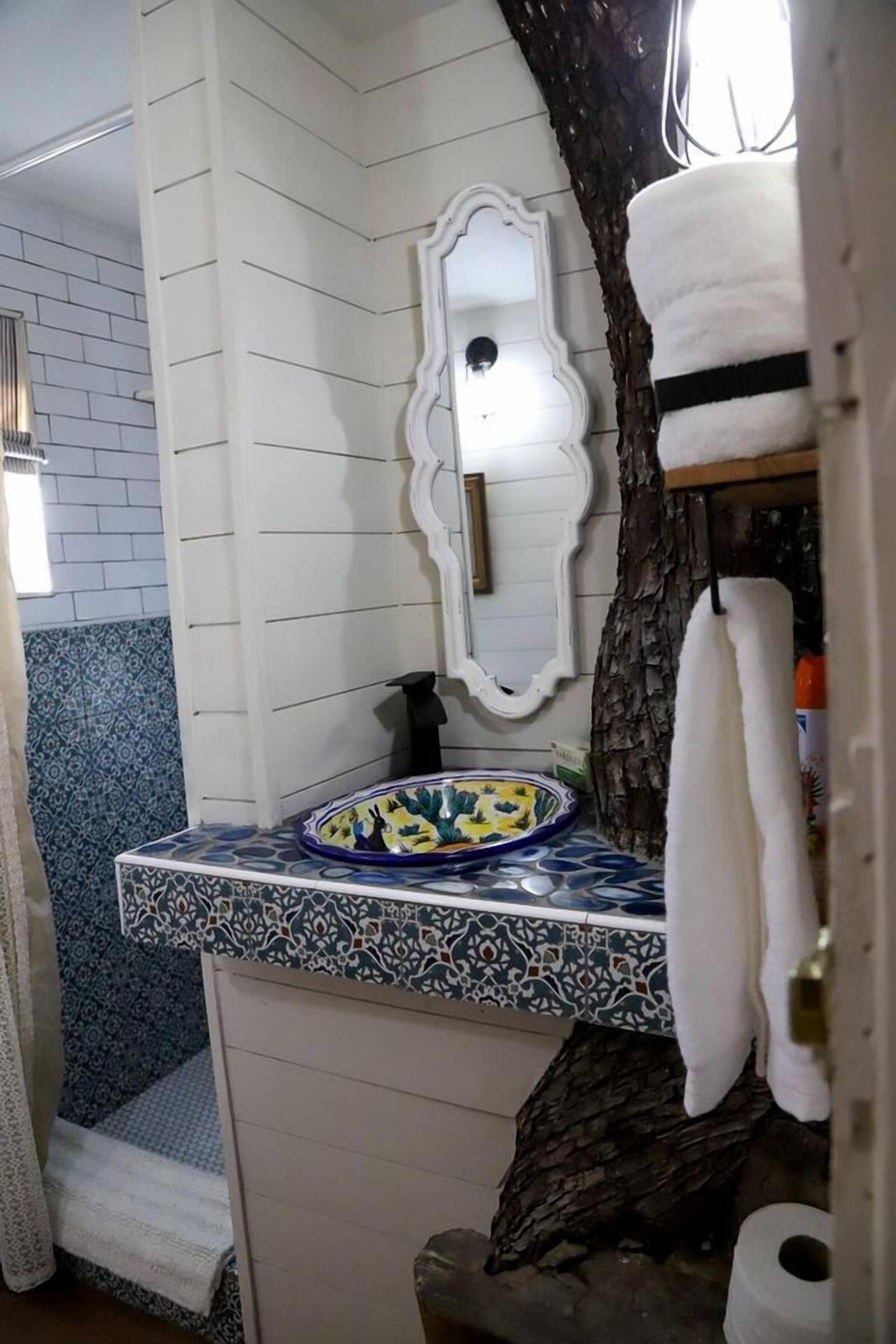 A bathroom with a white vanity, a decorative mirror, a patterned sink, and a tree trunk decoration.