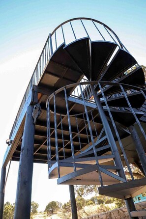 Una escalera de caracol con barandas metálicas y un cielo despejado al fondo.