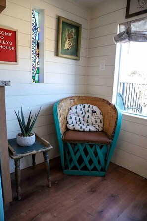 Una habitación de esquina con una silla de mimbre, una mesita con una planta y un ventanal con vistas.