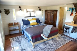 Un dormitorio con una cama, un aparador de madera, un banco, una mesita baja con taburetes y una lámpara de pared.