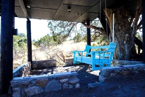 A covered outdoor seating area with a blue bench, stone walls, and a tree trunk.