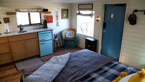 A cozy room with a bed, a small kitchenette, a chair, and a door.
