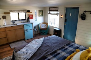 A cozy room with a bed, a small kitchenette, a chair, and a door.