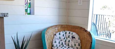 A corner room with a wicker chair, a small table with a plant, and a window with a view.