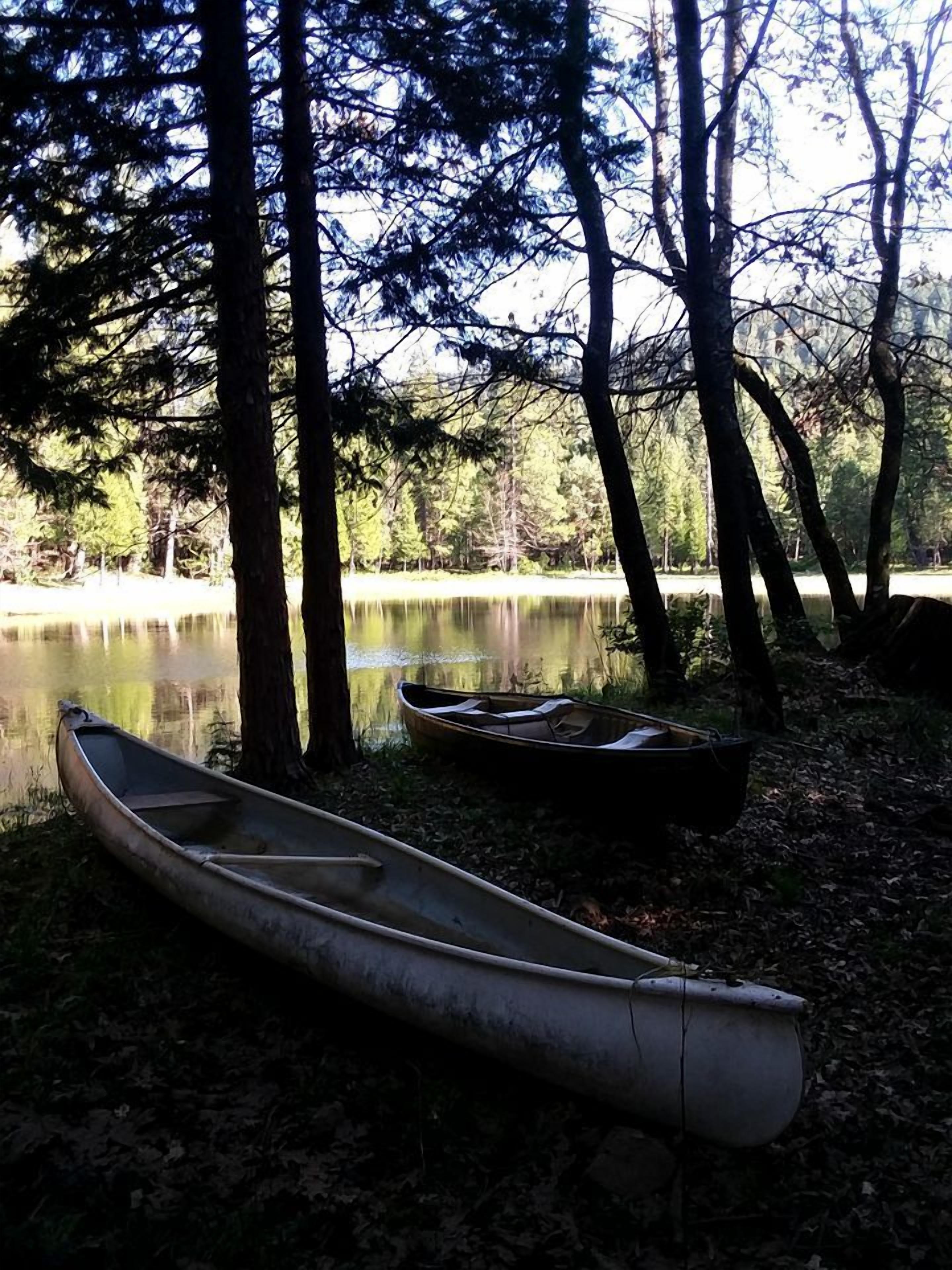 Una canoa y un kayak junto a un lago tranquilo rodeado de árboles.