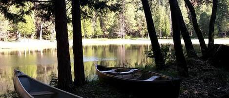 Una canoa y un kayak junto a un lago tranquilo rodeado de árboles.