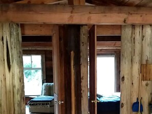 A rustic wooden room with a bed, a chair, and a window.