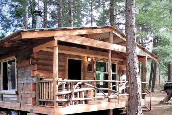 A rustic cabin with a porch, a chimney, and a door leading to the interior.
