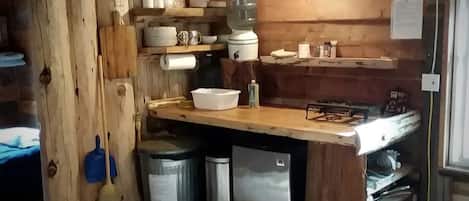 Une cuisine rustique avec des murs en bois, un plan de travail en bois, un évier, un réfrigérateur et un balai.