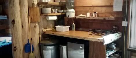 Una cocina rústica con paredes de madera, una encimera de madera, un lavamanos, un refrigerador y una escoba.