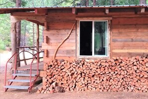 A wooden cabin with a window, a set of stairs, and a stack of firewood.