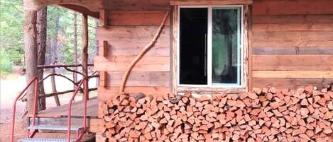 Una cabaña de madera con una ventana, unos escalones y una pila de leña.