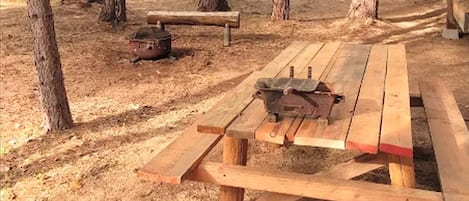 Une table de pique-nique avec un barbecue portable et un banc, le tout installé dans un espace boisé.