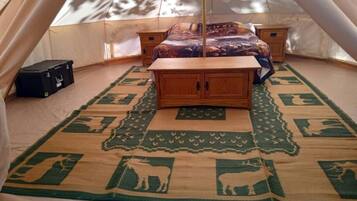 Una carpa con una cama, un mueble de madera y una alfombra estampada.