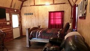 A log cabin bedroom with a bed, leather sofa, wooden walls, and a red curtain.