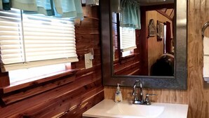 A bathroom with wooden paneling, a white sink, a mirror, and a window with blinds.