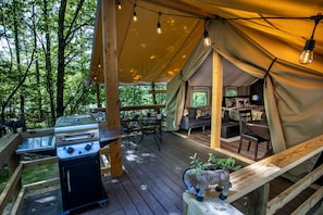 Un espace extérieur aménagé avec une tente, un barbecue, une terrasse en bois et une table à manger.
