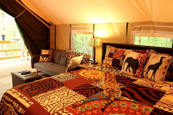 A tented room with a bed, a sofa, a lamp, and a view of the outdoors.