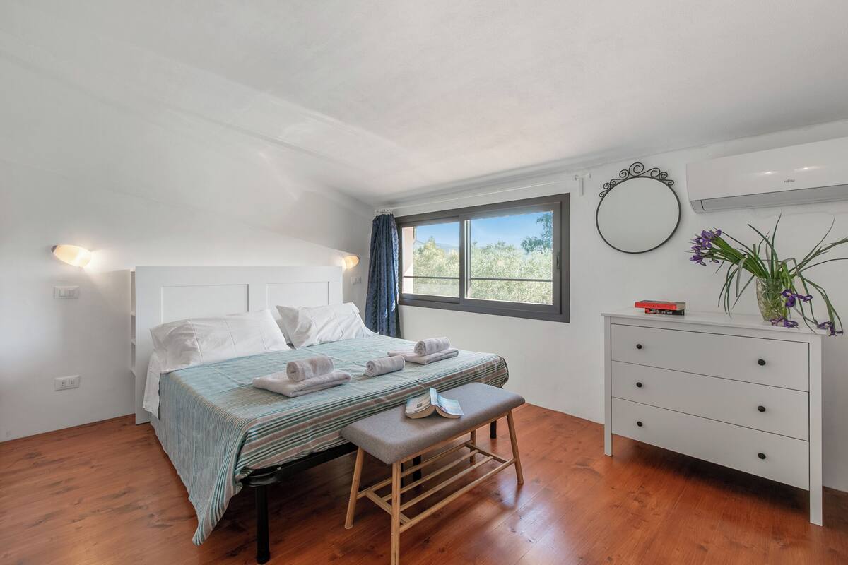 A bedroom with a bed, bedside table, dresser, and a window with a view.