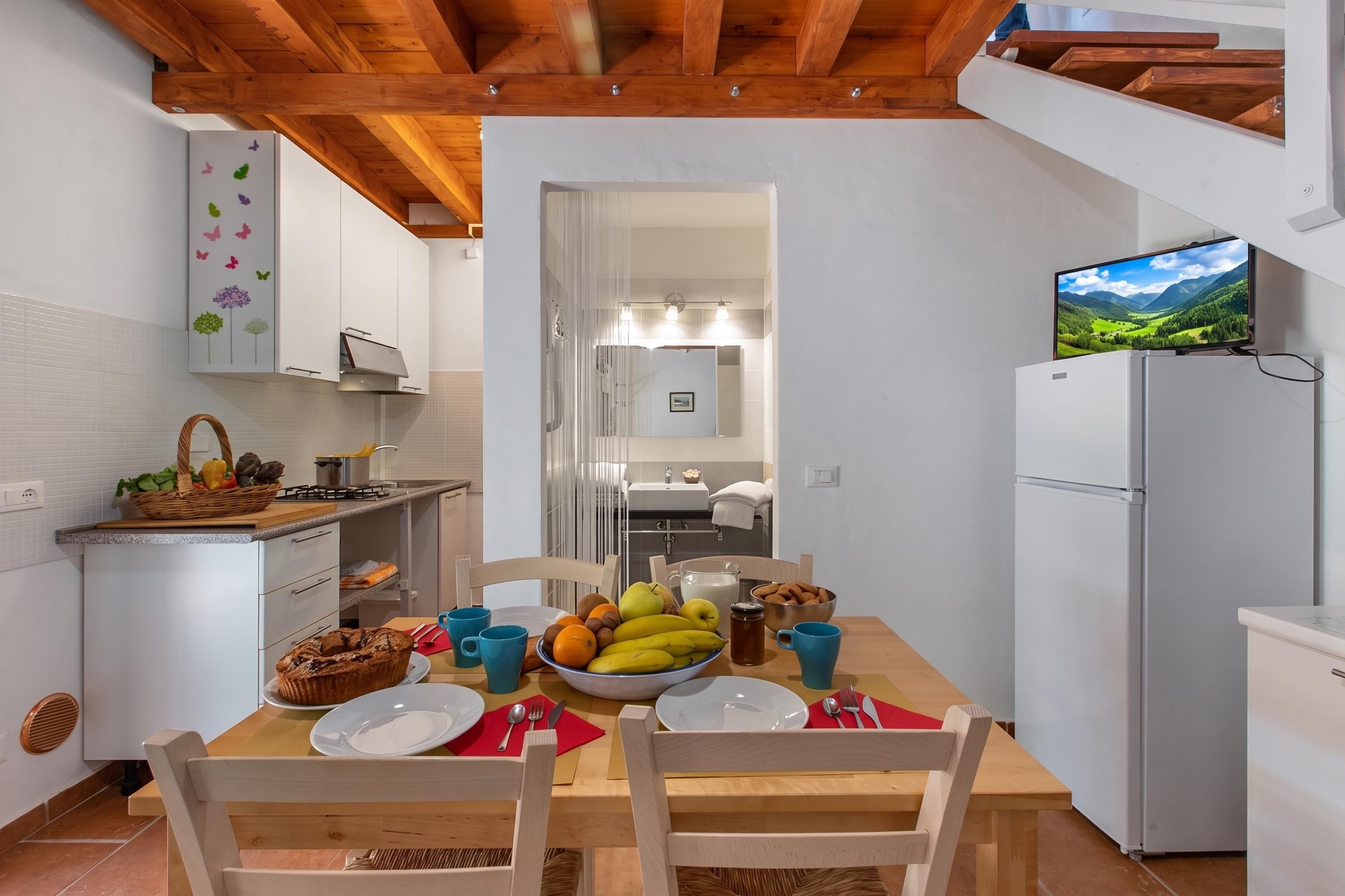 Een moderne keuken met witte kastjes, een eettafel gedekt voor vier personen en een aan de muur bevestigde televisie.