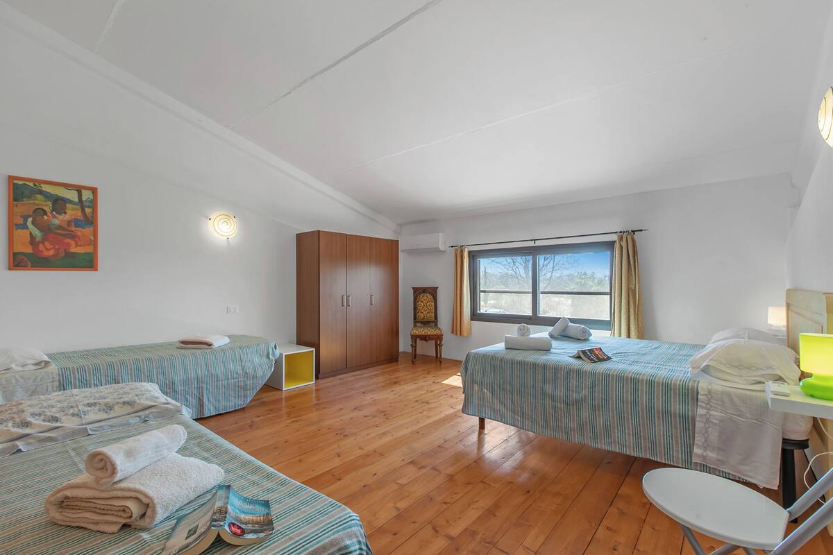 A room with two beds, a wooden wardrobe, a chair, a desk with a lamp, and a window with curtains.