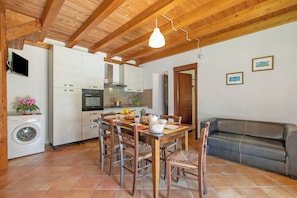 A kitchen with wooden beams, a dining table with chairs, a washing machine, and a sofa.