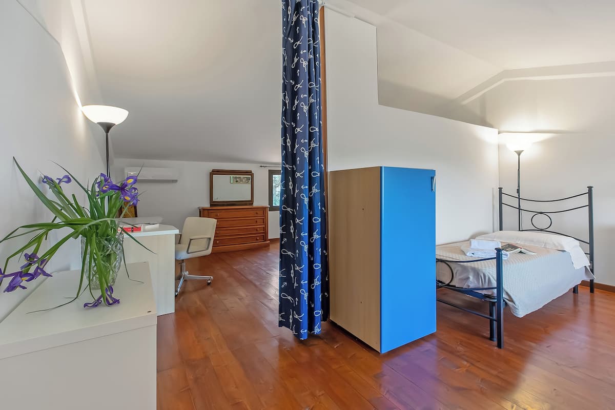 A room with a bed, a desk, a chair, a lamp, and a plant.