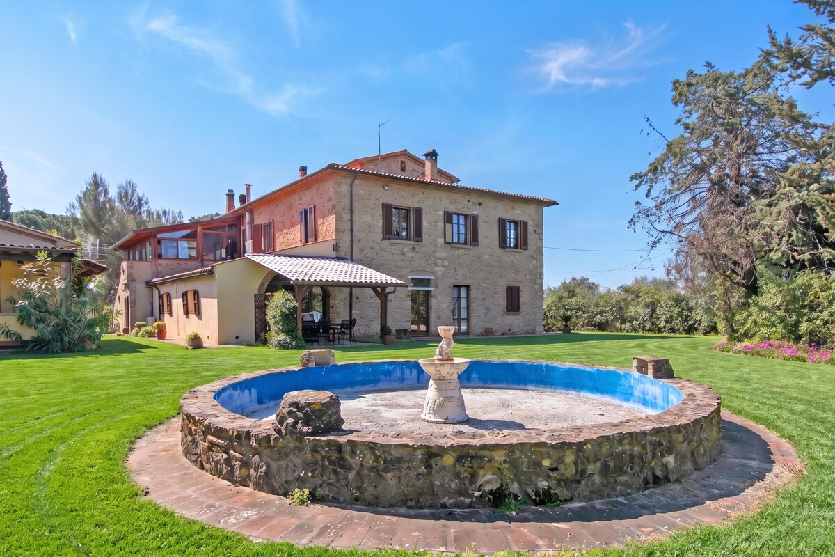 A two-story stone house with a swimming pool and a fountain.