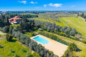 A large property with a swimming pool, surrounded by lush greenery and a view of the countryside.