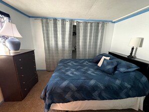 Une chambre à coucher avec un lit, une commode, une table de chevet et une fenêtre avec des rideaux.