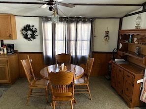 Un coin repas comprenant une table ronde en bois, quatre chaises, un ventilateur de plafond et une fenêtre avec des rideaux.