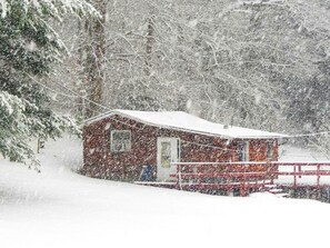 A snow-covered cabin with a red roof and a small porch.