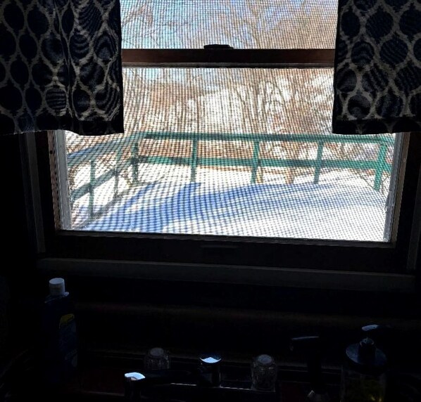 A window with a view of a green bench and a patterned curtain.