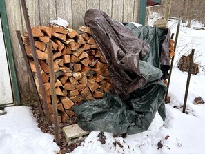 A stack of firewood and a green tarp in a snowy outdoor setting. - Rustic Cabin Rental near Akron, Ohio (Dellroy)