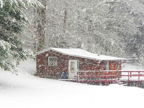 A snow-covered cabin with a red roof and a small porch. - Rustic Cabin Rental near Akron, Ohio (Dellroy)