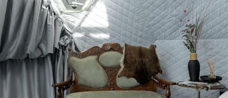 Une pièce avec un plafond matelassé, un canapé ancien, une petite table sur laquelle est posé un vase, et un tapis en fourrure.