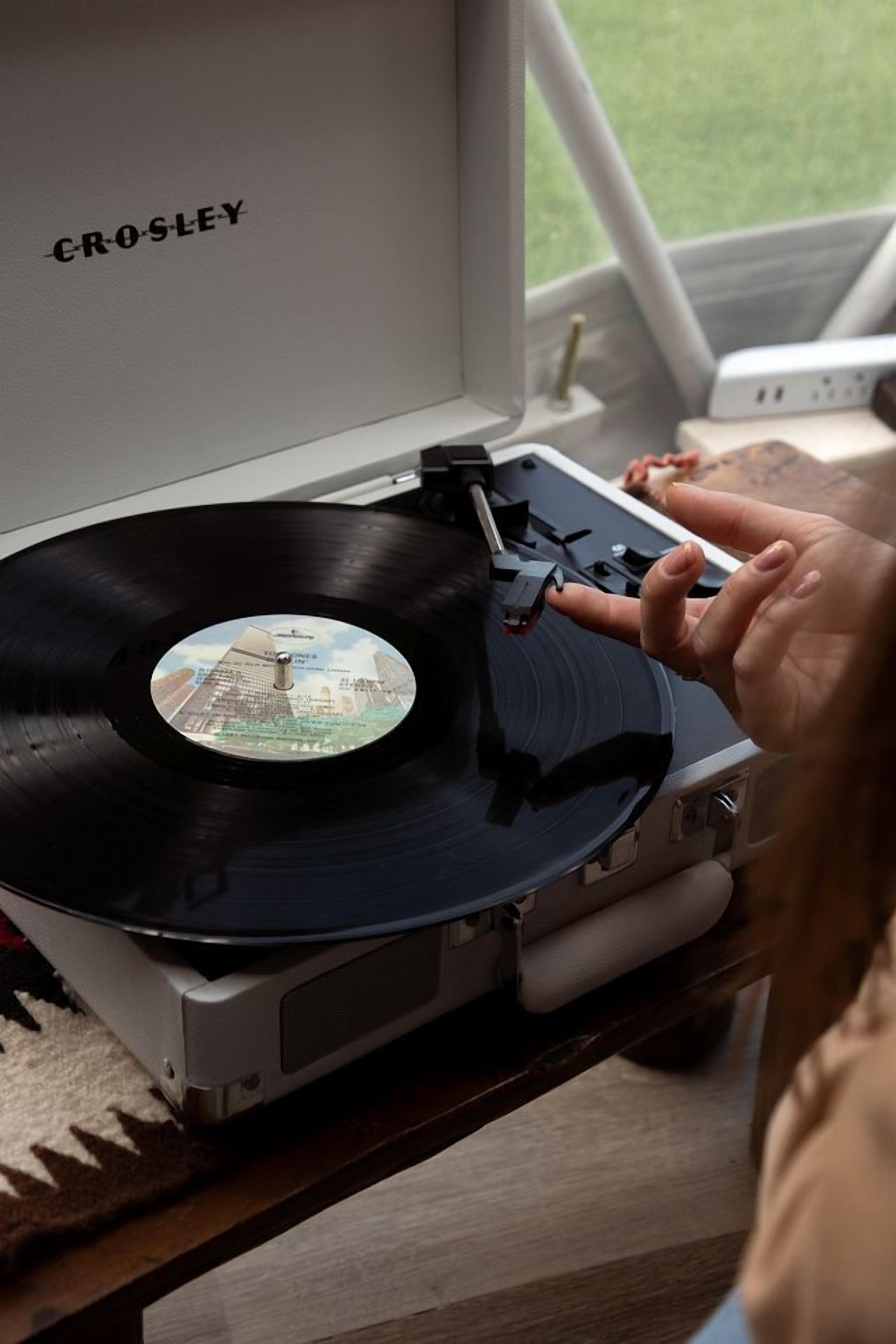 A turntable with a vinyl record, a person's hand, and a window with a view of a grassy area.