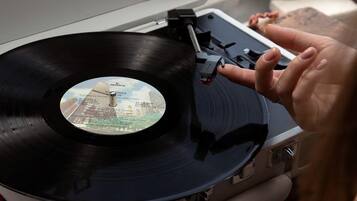 A turntable with a vinyl record, a person's hand, and a window with a view of a grassy area.
