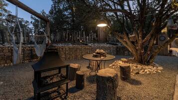 An outdoor seating area with a table and benches, surrounded by trees and a stone wall.